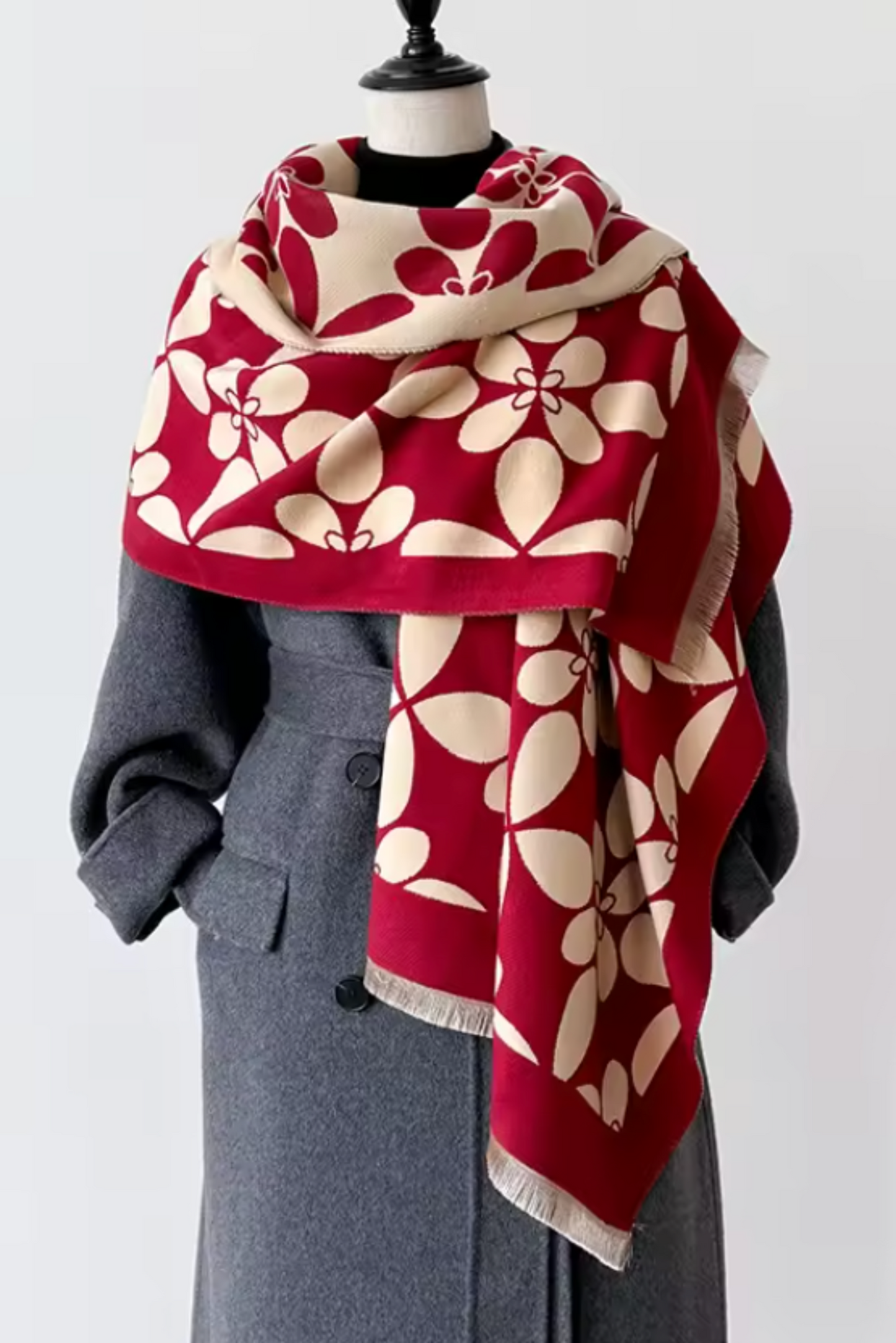 A red and beige floral patterned scarf styled on a black mannequin torso wearing a gray coat, against a plain light gray background.