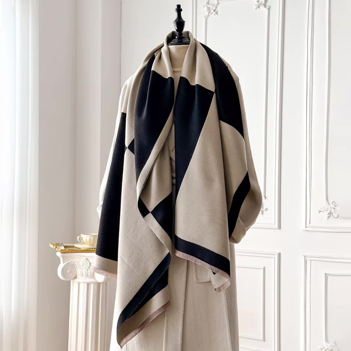 Beige and black striped scarf on a mannequin against a white paneled wall.