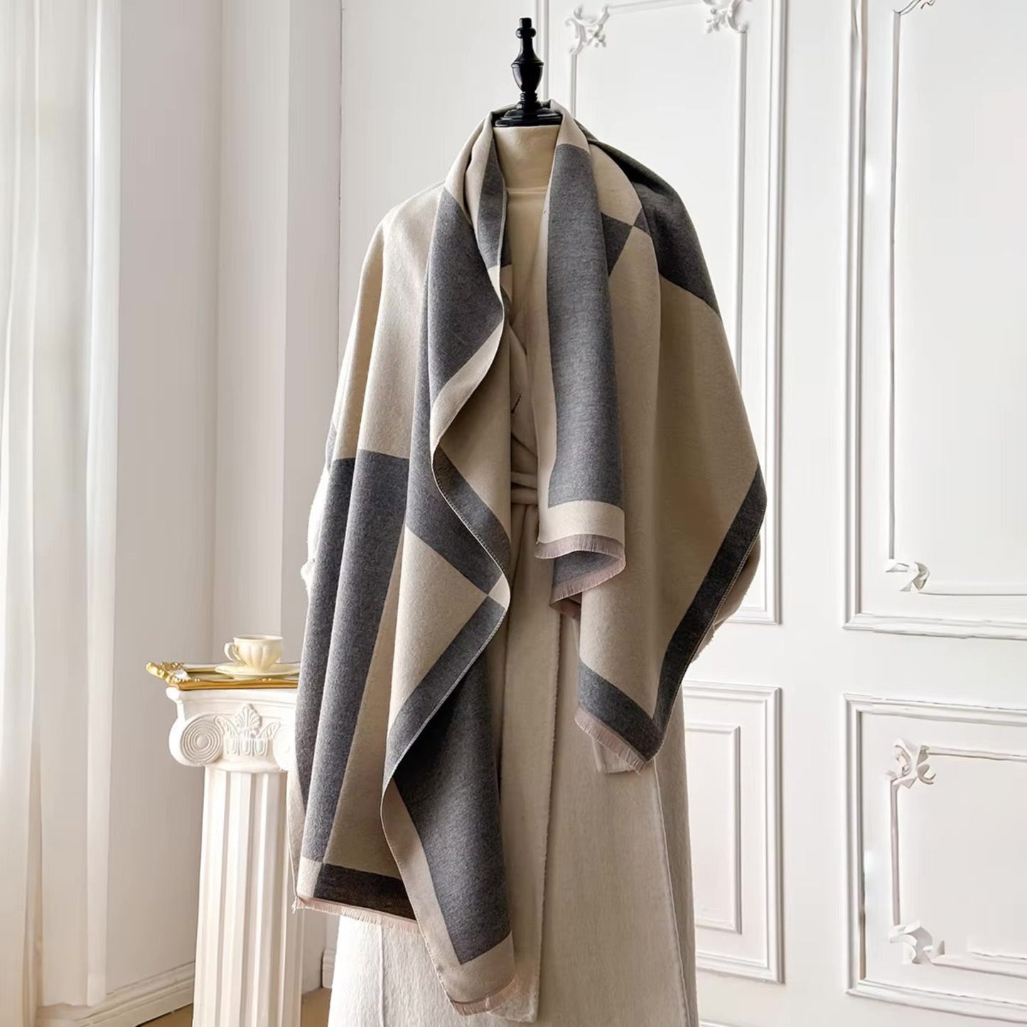 Mannequin wearing a beige and gray striped scarf against a white wall.