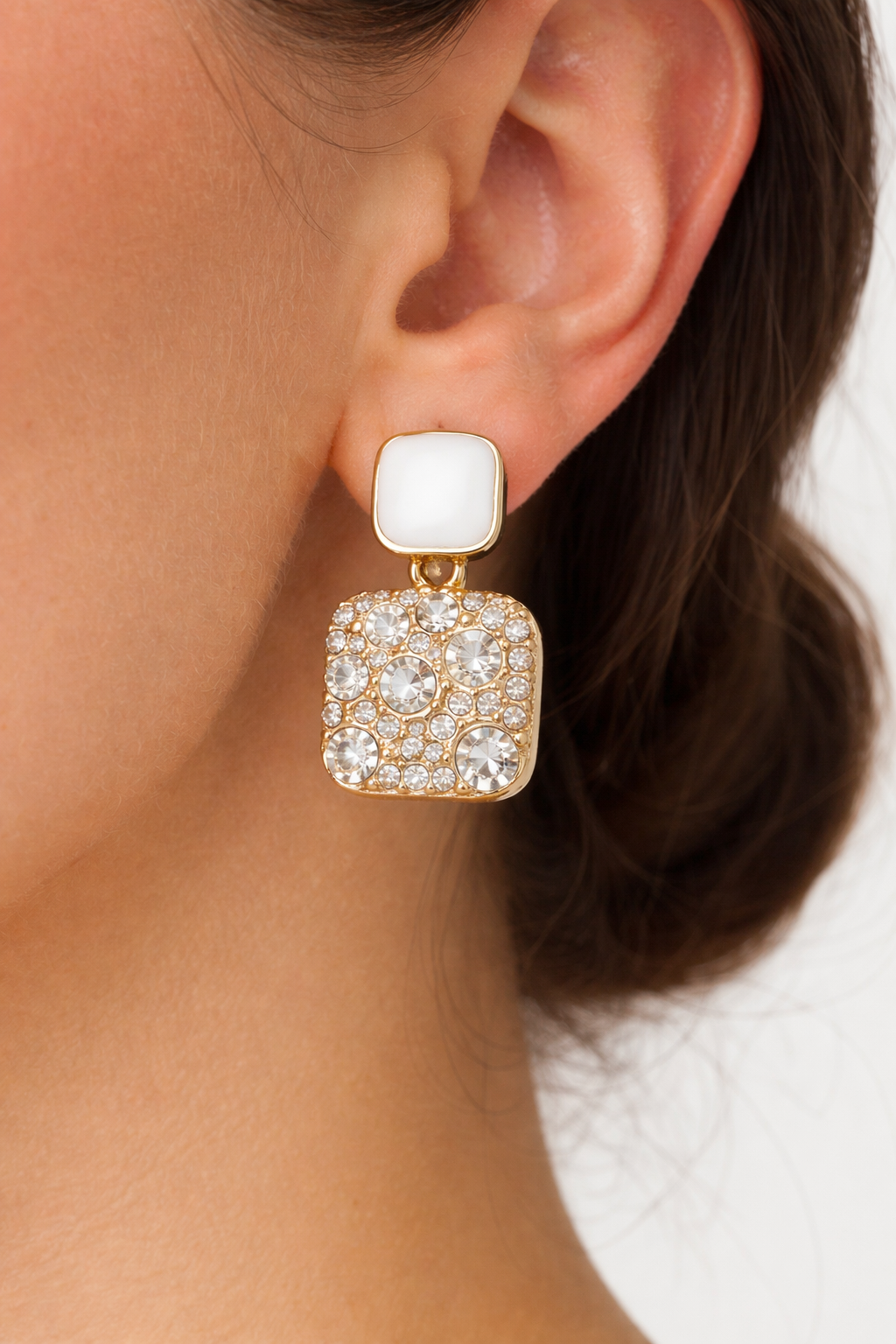 Close-up of a woman wearing a gold and crystal earring with a white background