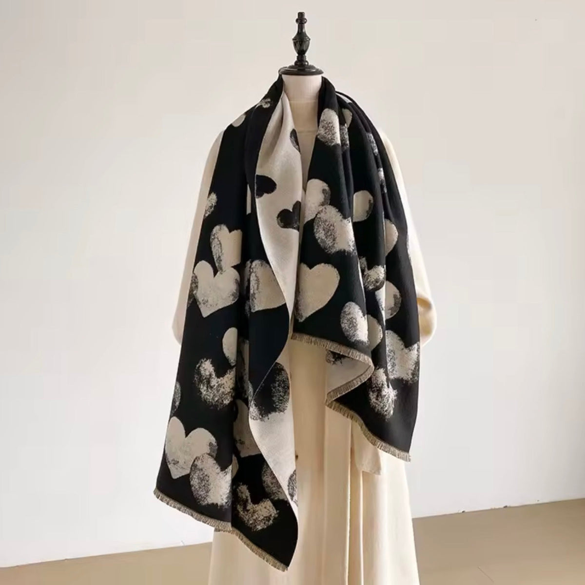 A black and cream scarf with a heart pattern draped over a cream-colored dress form against a plain off-white background.