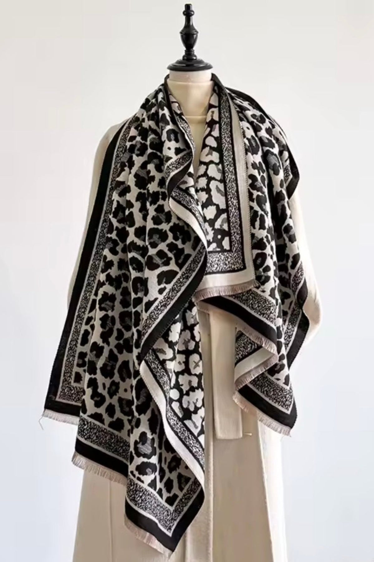 A black and off-white leopard print scarf with ornate borders, draped on a cream-colored mannequin dress form against a plain white background.