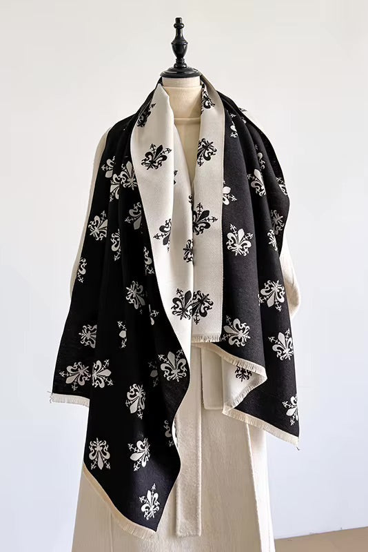 A black and off-white patterned shawl with white floral motifs is draped over a cream-colored dress form against a plain white wall.