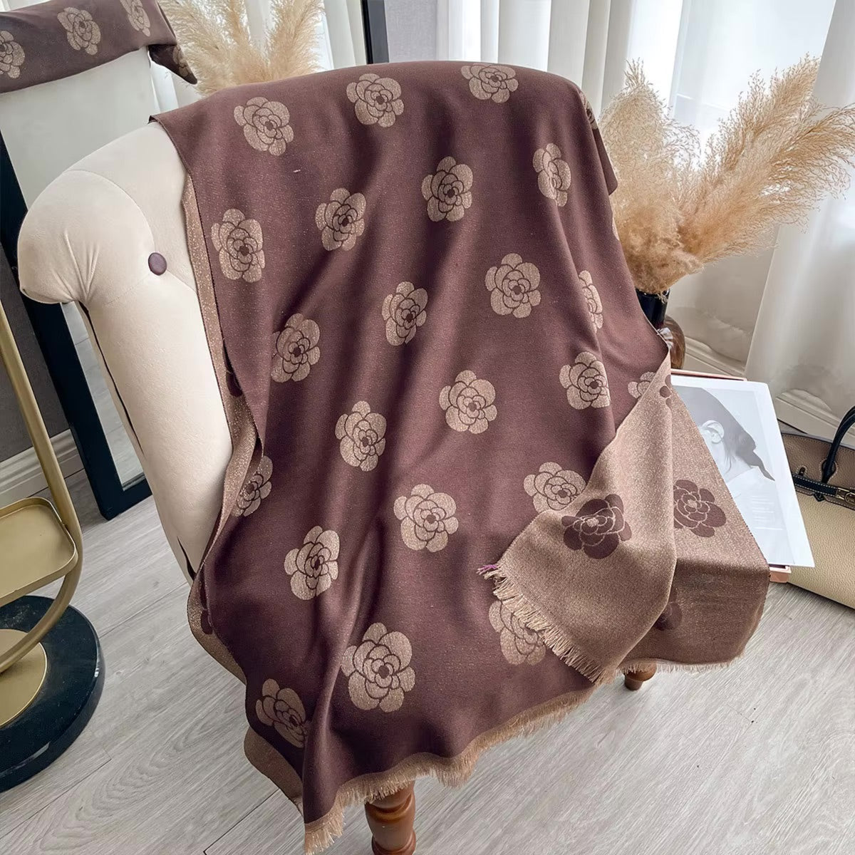 A brown throw blanket with a beige floral pattern draped over a cream-colored armchair in a styled room setting.