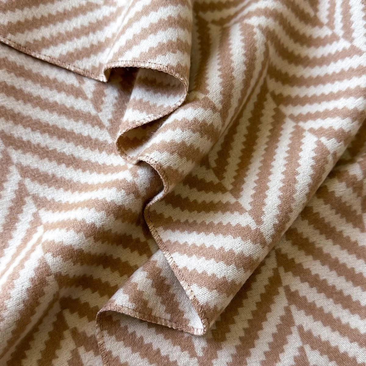 A close-up of draped fabric with a repeating chevron pattern in warm tan and off-white.