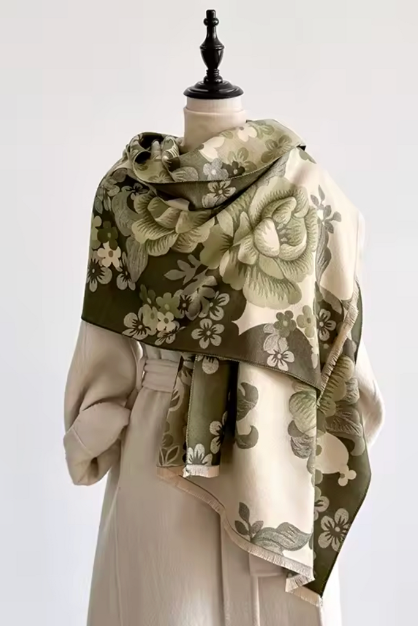 A cream-colored silk scarf with an olive green floral pattern, elegantly draped over a beige dress on a mannequin against a plain white background.