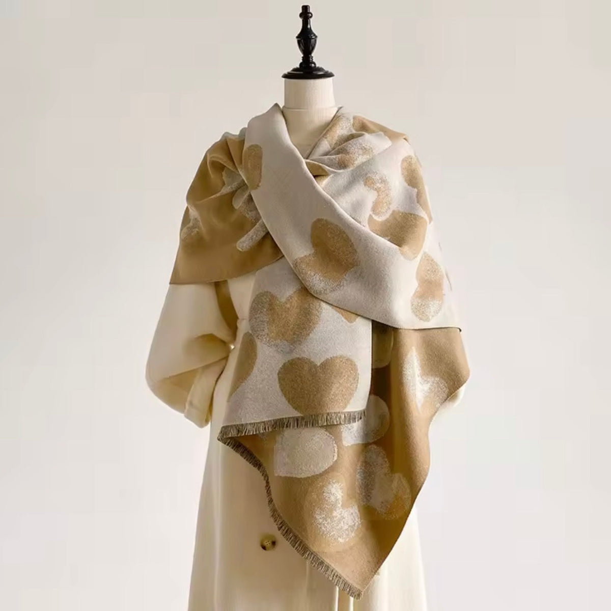 A cream and beige shawl with metallic gold heart motifs draped on a cream-colored mannequin dress form against a light off-white background.