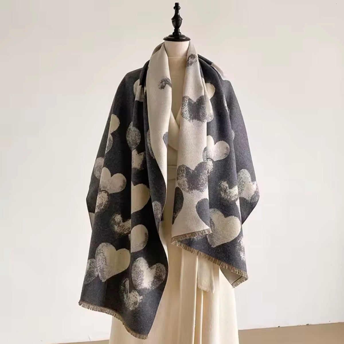 A cream and dark gray scarf with a heart pattern draped over a cream-colored dress form against a plain off-white background.
