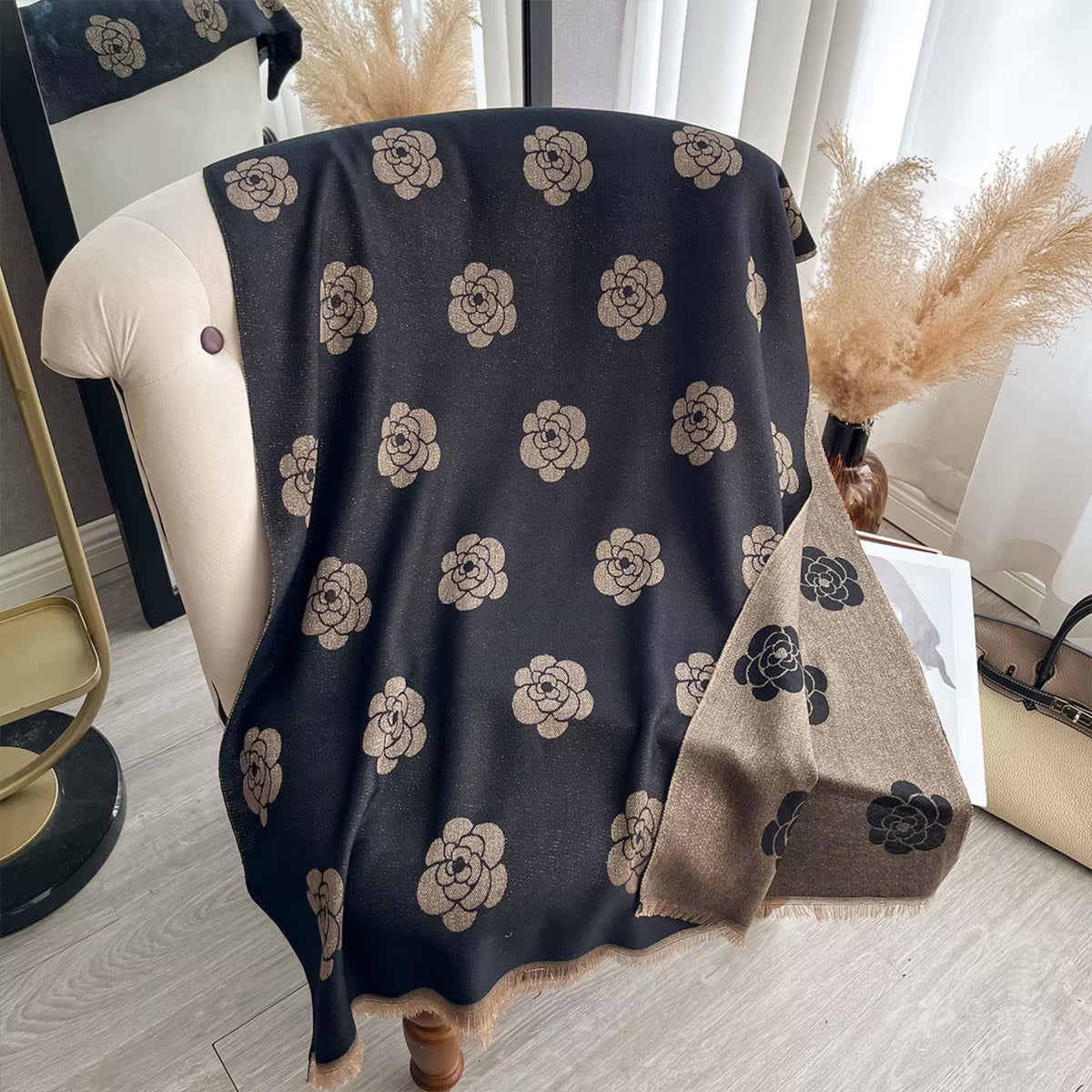 A dark charcoal gray throw blanket with a beige floral pattern draped over a cream-colored armchair in a styled room setting.