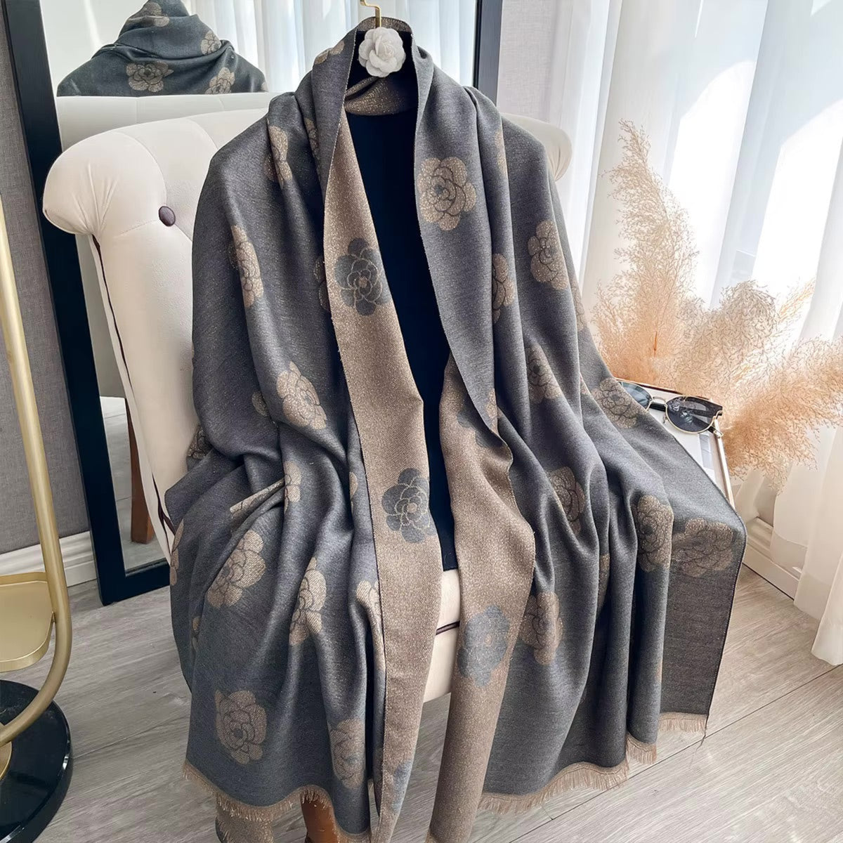 A gray and beige shawl with a floral pattern draped over a chair in a bright room.