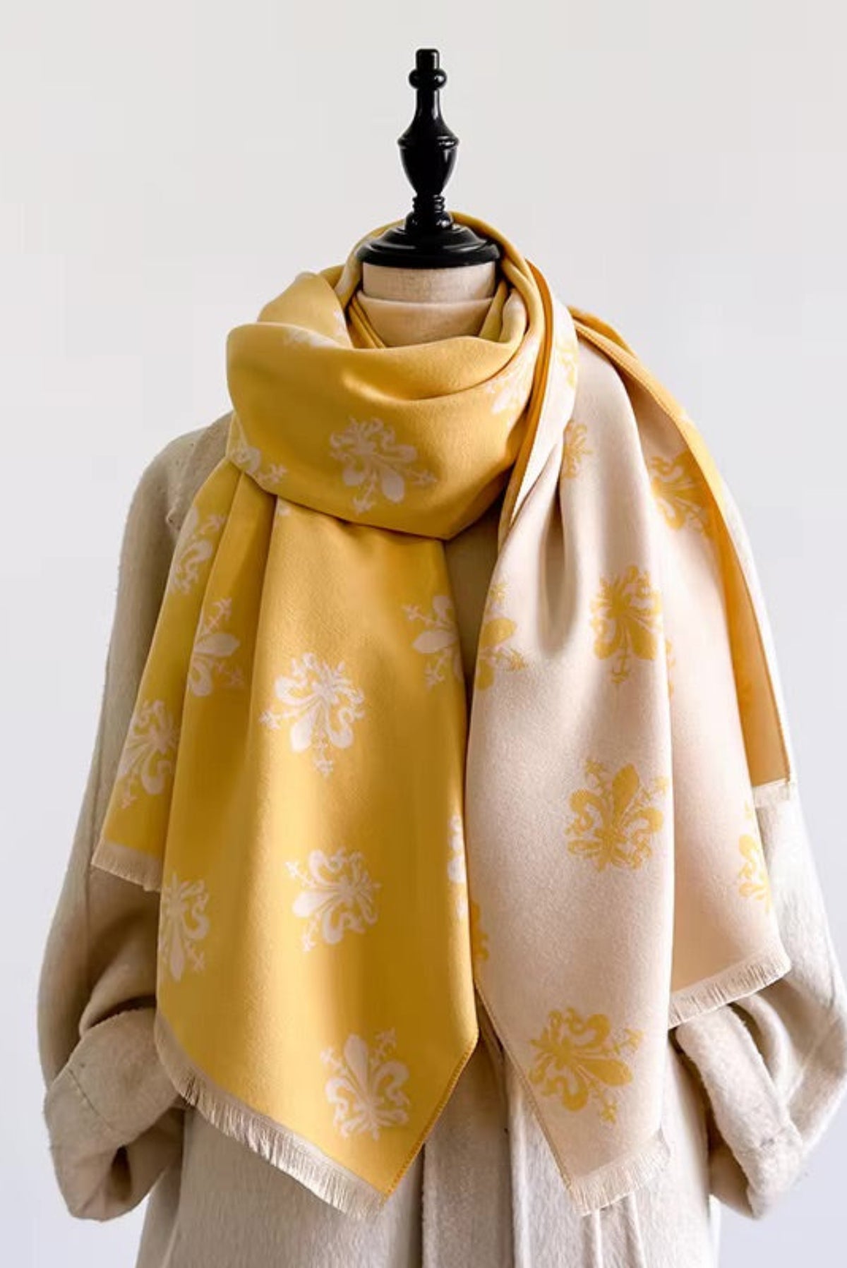 A large mustard yellow and cream scarf with white floral motifs, draped over a beige dress form against a plain white background.