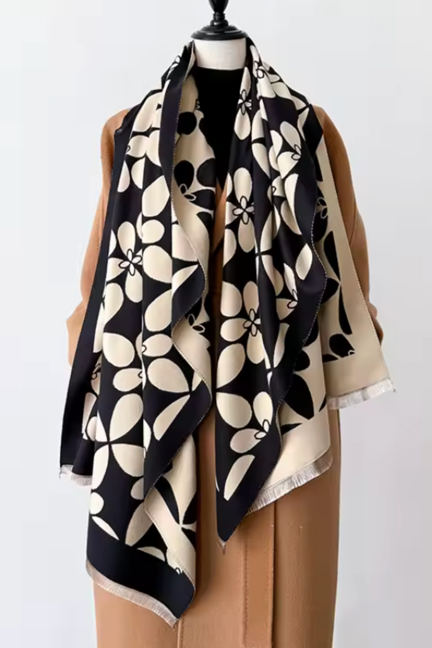 A large square scarf with a bold black and cream floral pattern, draped on a tan mannequin torso against a plain light gray background.