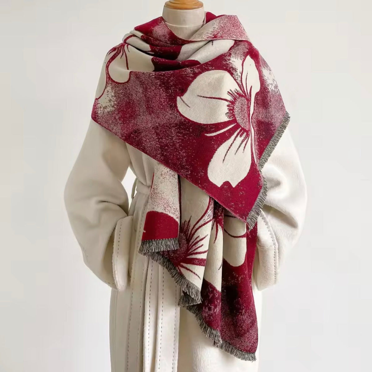 A large square scarf with a bold floral pattern in deep burgundy and cream, styled on a cream-colored coat dress form against a plain white background.
