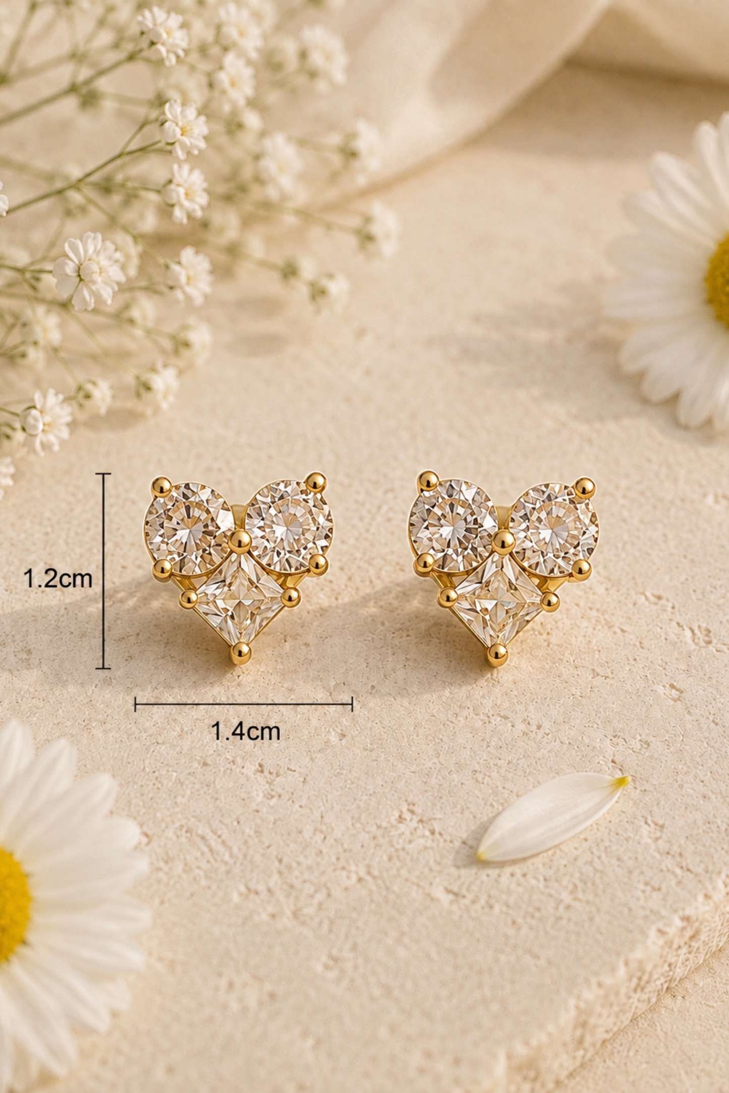 A pair of gold-tone stud earrings with clear gemstones, displayed on a textured beige surface with daisy flowers and baby's breath. Black measurement lines and text indicate dimensions of 1.