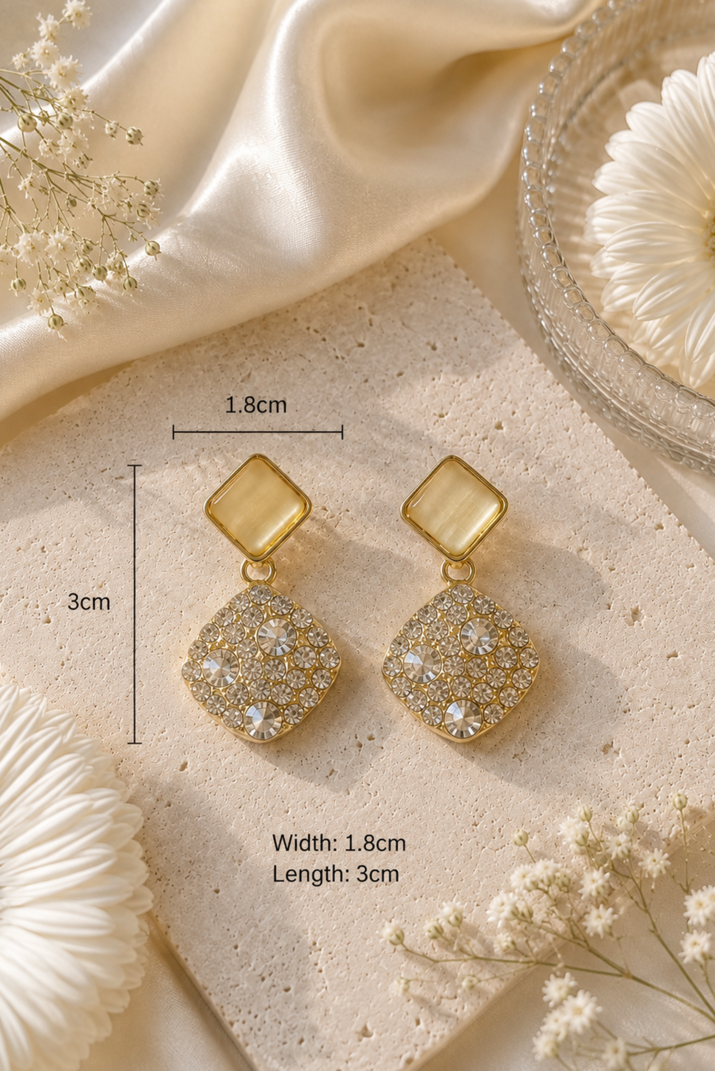 A pair of gold-toned square drop earrings with textured crystal-like lower sections, displayed on a beige stone slab with overlaid dimension labels showing 1.8cm width and 3cm length.