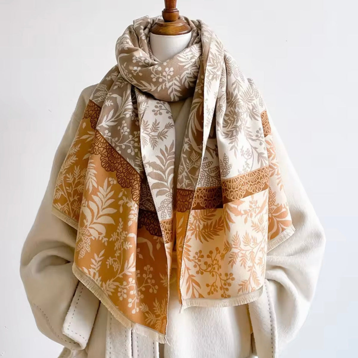 A patterned scarf draped on a cream-colored coat displayed on a mannequin torso against a plain white background.