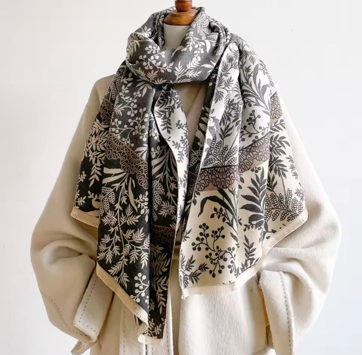 A patterned scarf draped over a cream-colored coat on a mannequin torso against a plain white background.