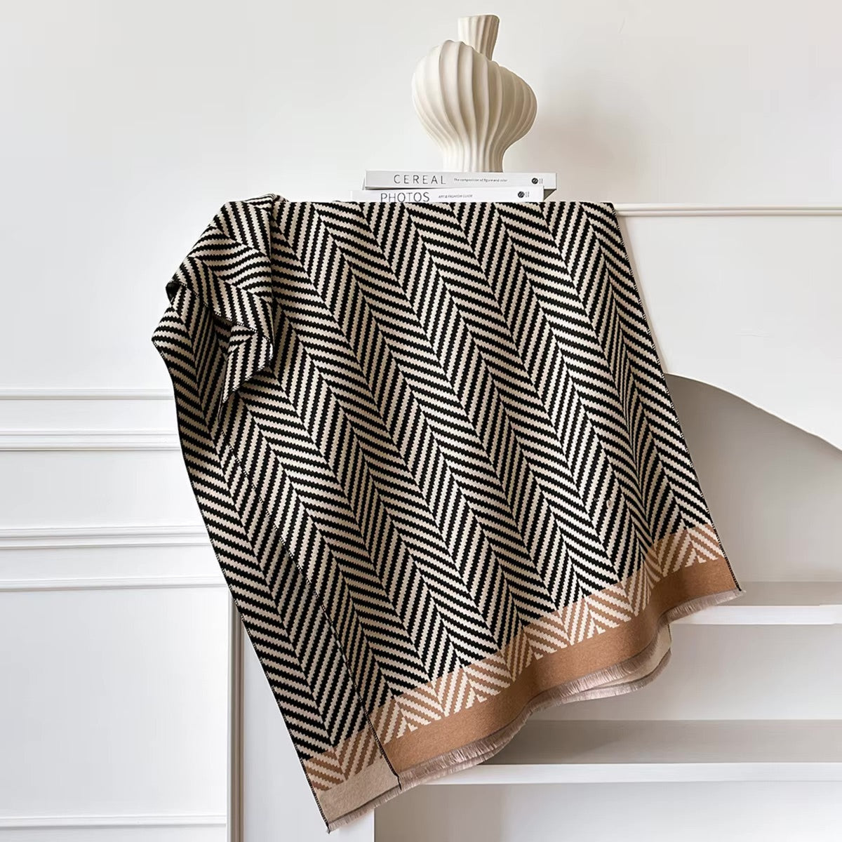 Black and white patterned scarf with gold trim draped over a white surface.