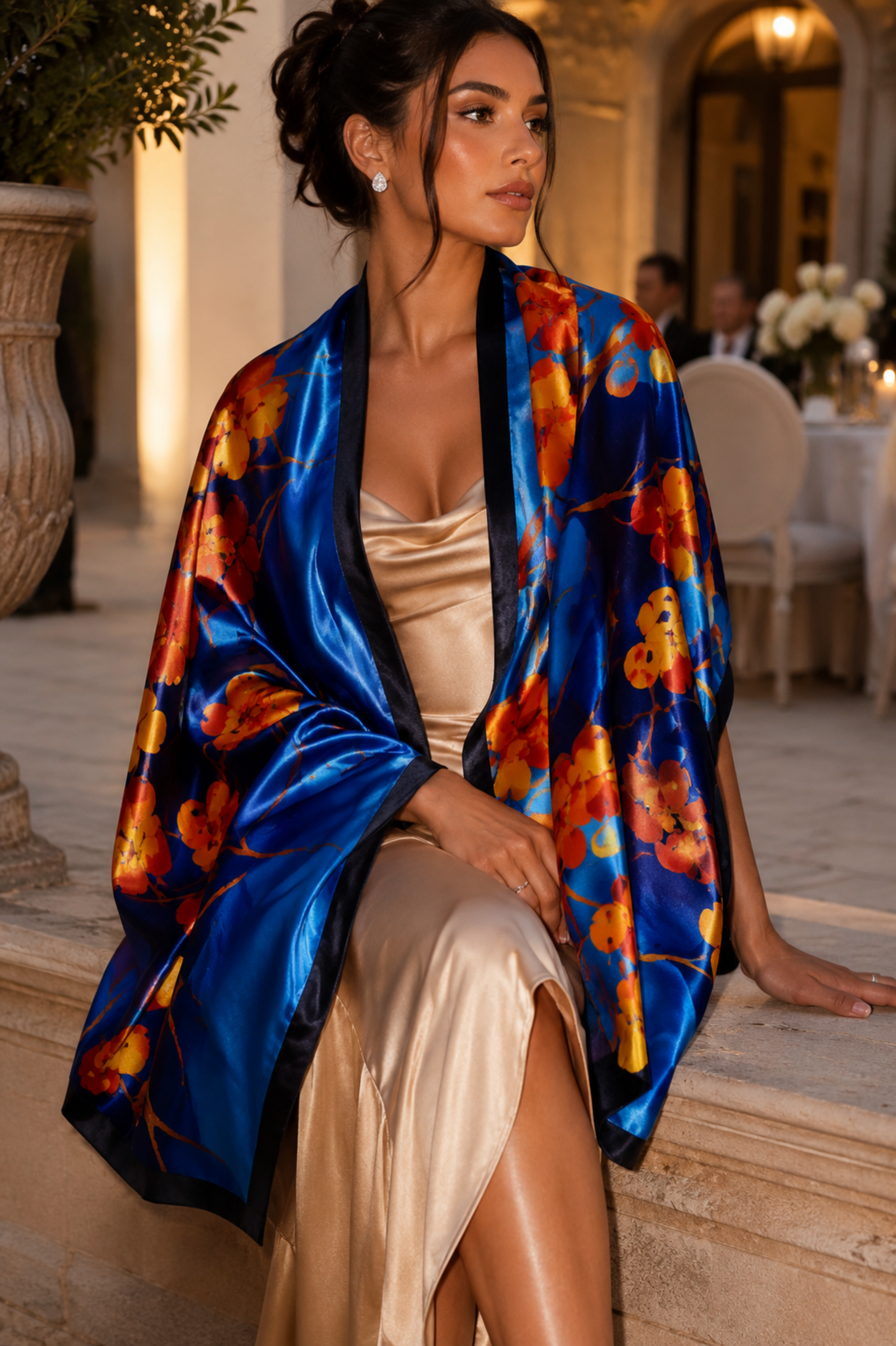 Woman wearing a colorful floral kimono over a beige dress in an elegant outdoor setting.