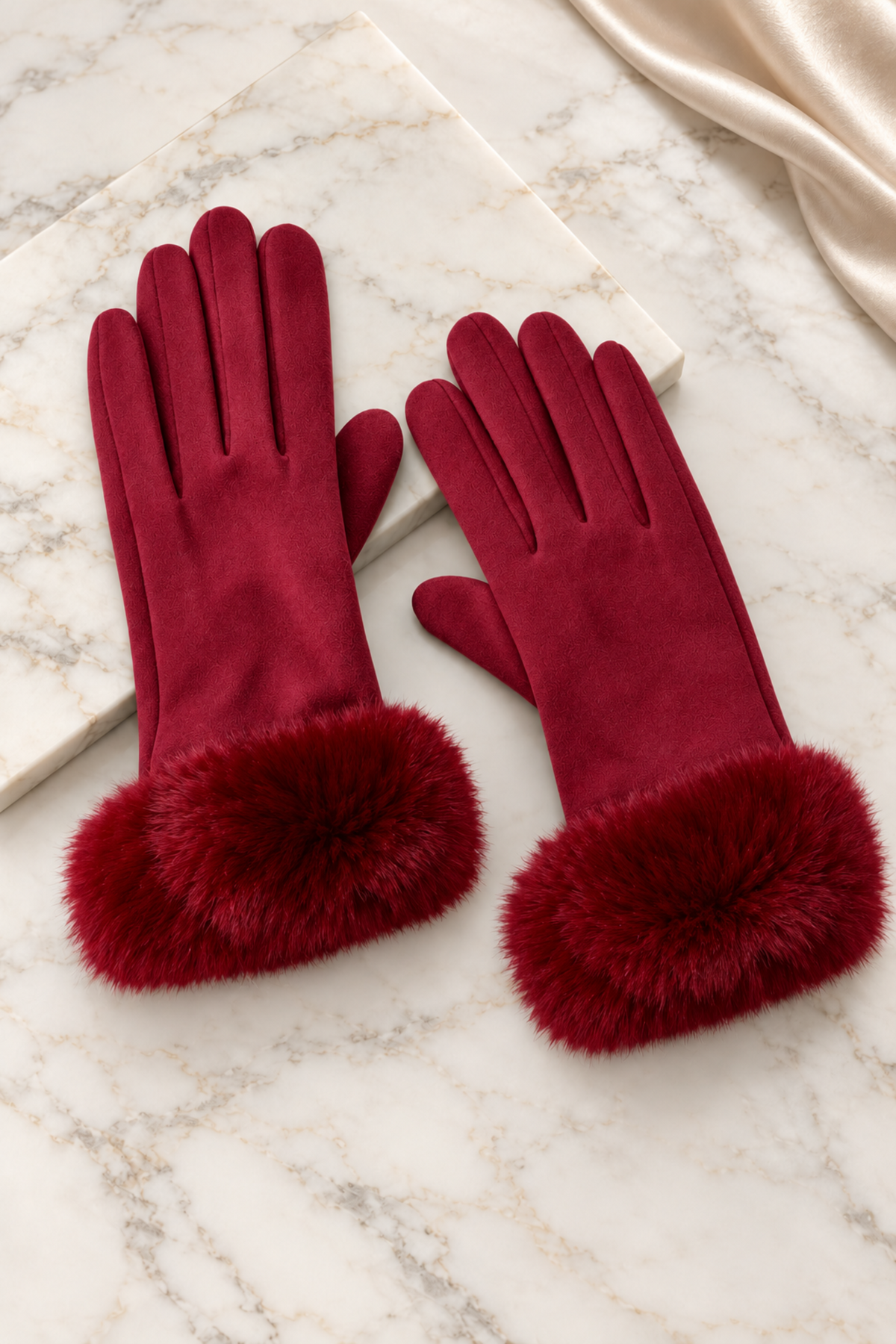 A pair of deep burgundy gloves with fluffy faux fur trim at the cuffs, displayed on a white marble surface.