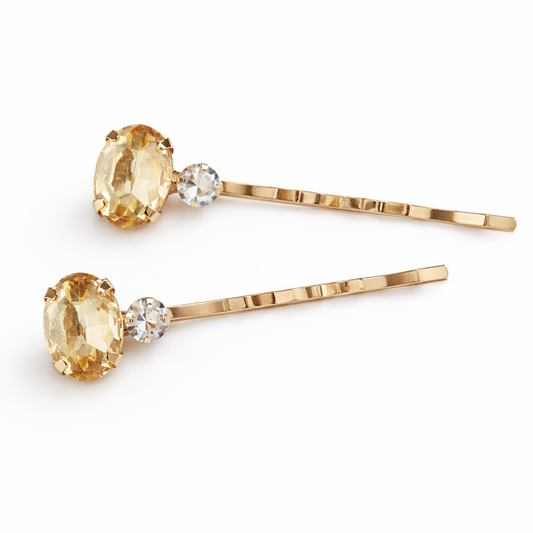 Two gold hair pins with yellow gemstones on a white background