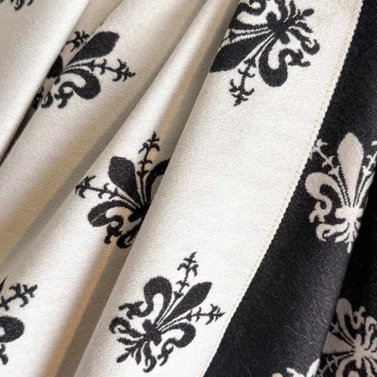 Close-up of a patterned fabric with black damask-style floral motifs on an off-white background, plus a black vertical border stripe.