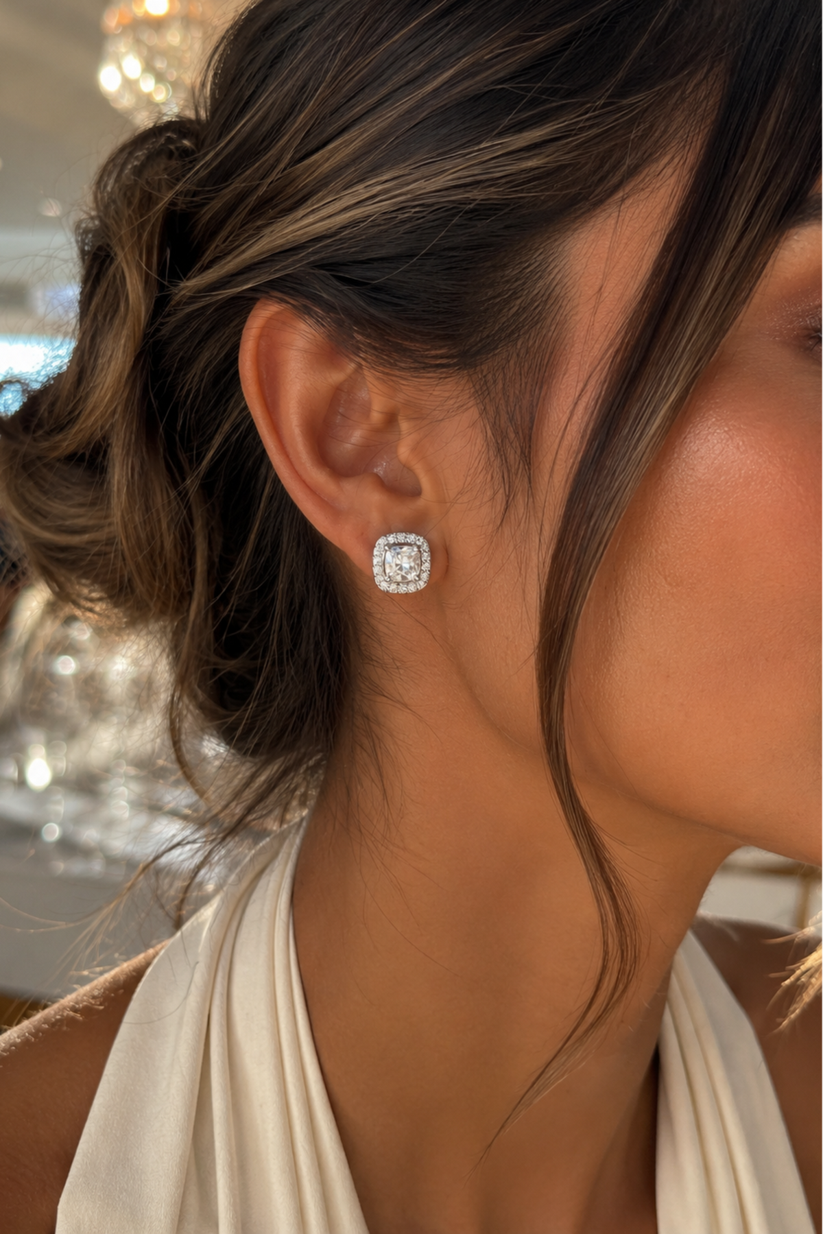 Close-up of a person wearing diamond stud earrings with a blurred indoor background.