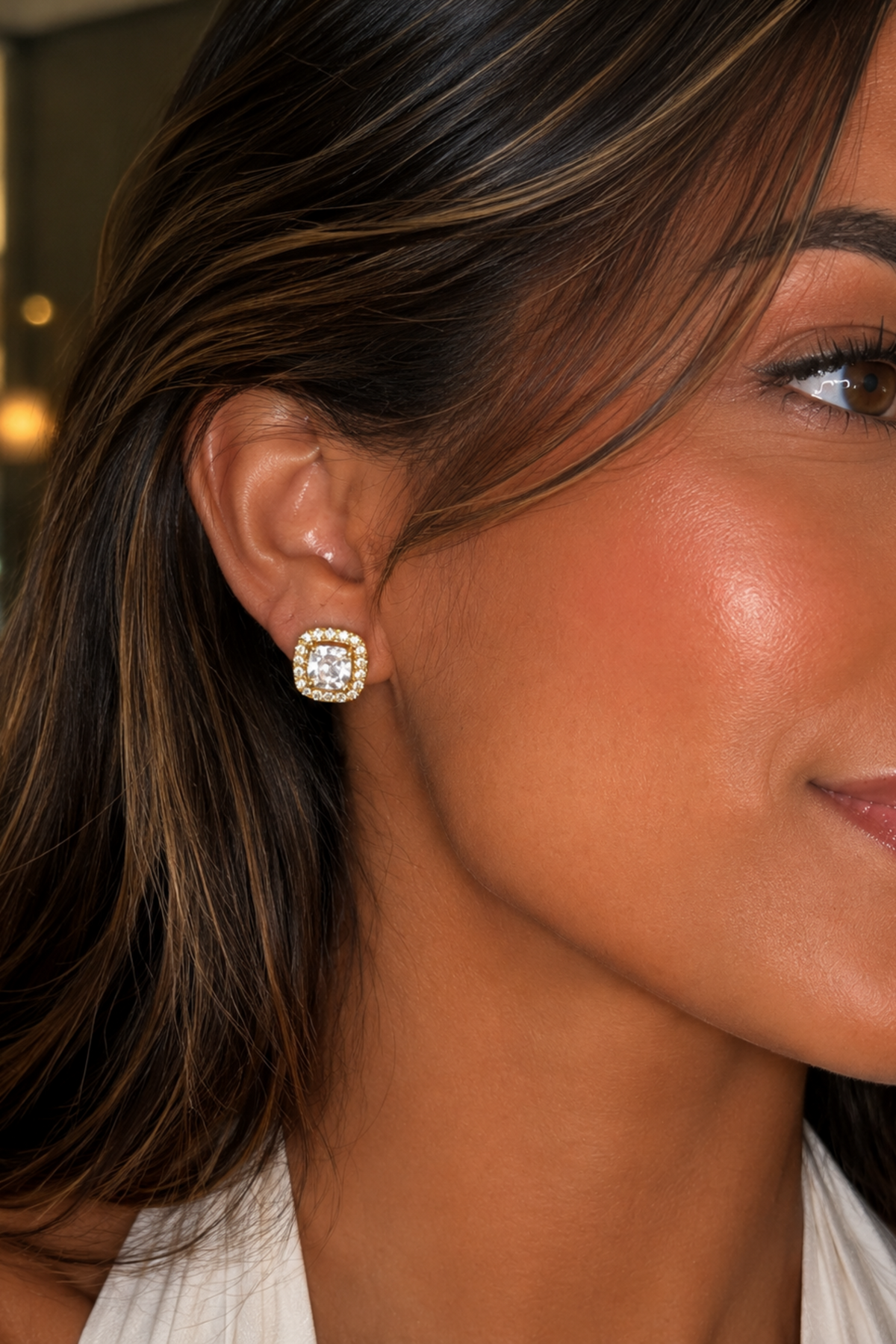Close-up of a woman wearing a gold earring with a clear gemstone.
