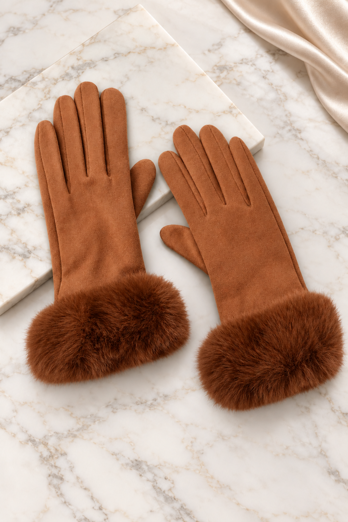 A pair of warm brown faux-suede gloves with fluffy faux-fur cuffs, displayed on a white marble surface.