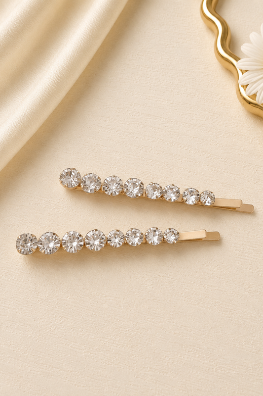 Two gold hair pins with clear crystals on a beige fabric background