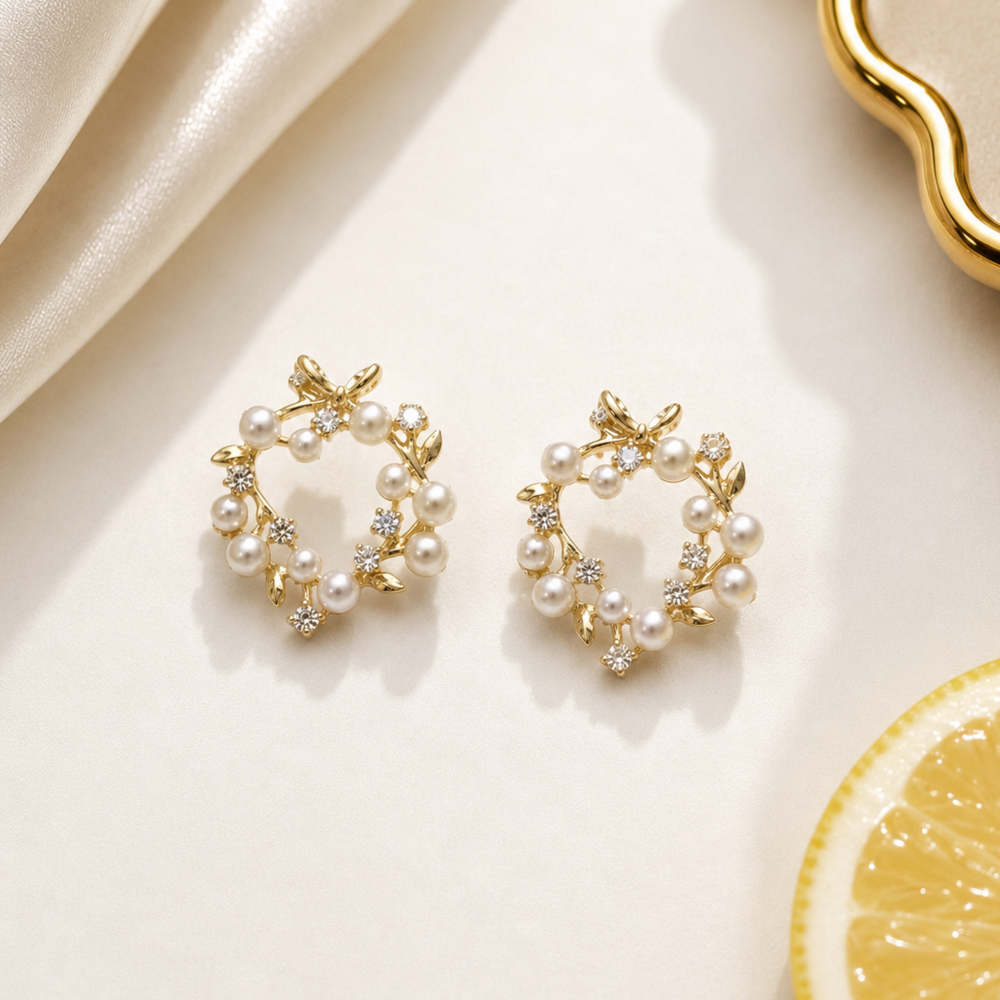 Gold and pearl earrings on a light background with a lemon slice