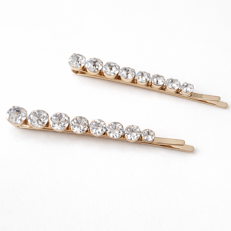 Two gold hair pins with clear crystals on a white background