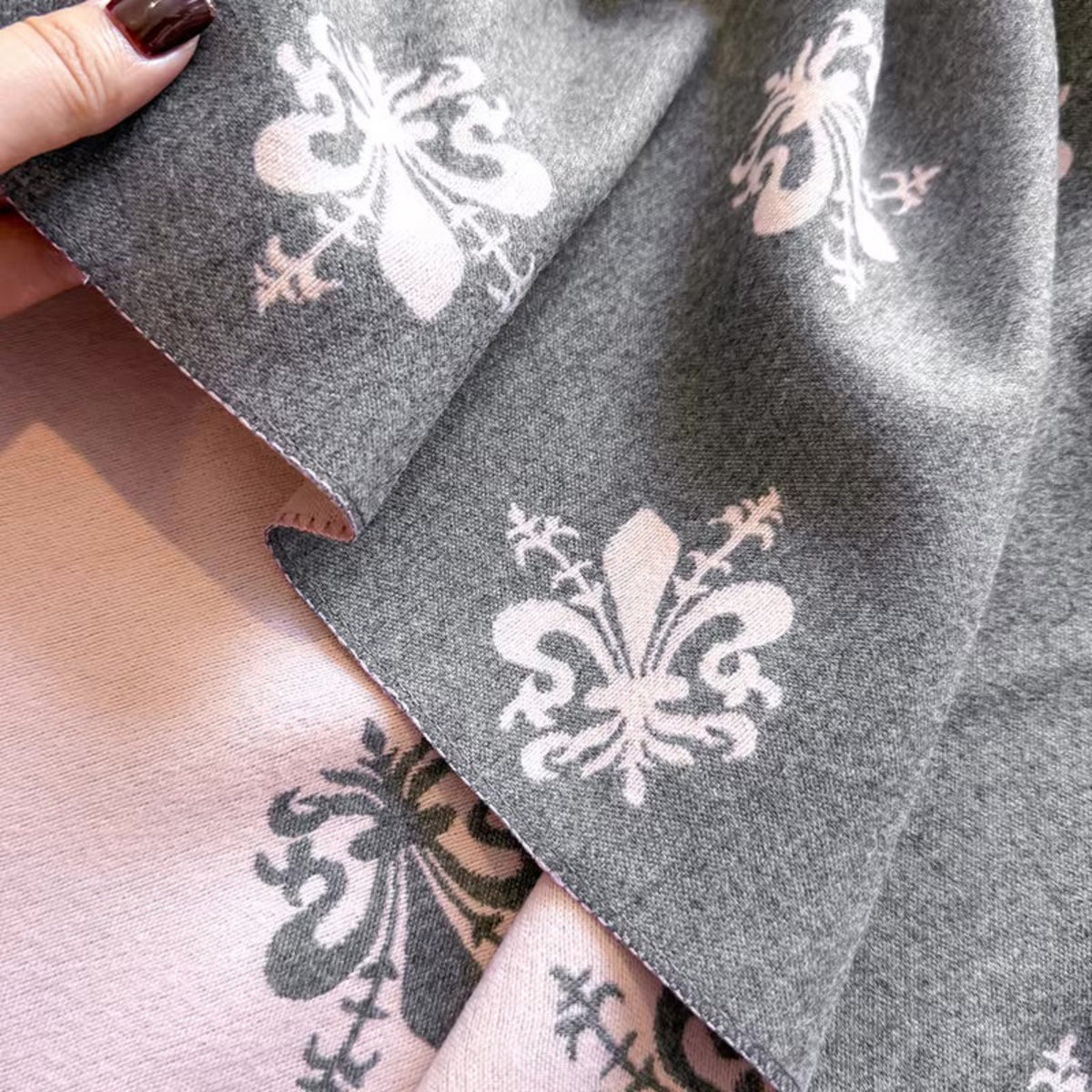 Gray fabric with white floral patterns held by a hand with dark nail polish.