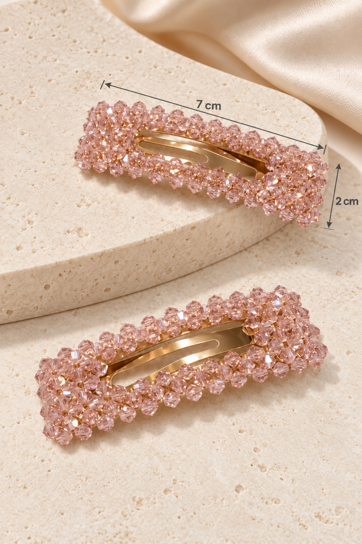 Two pink rhinestone hair clips with gold-tone metal bars, shown on a beige textured surface with dimension annotations indicating 7 cm length and 2 cm height.