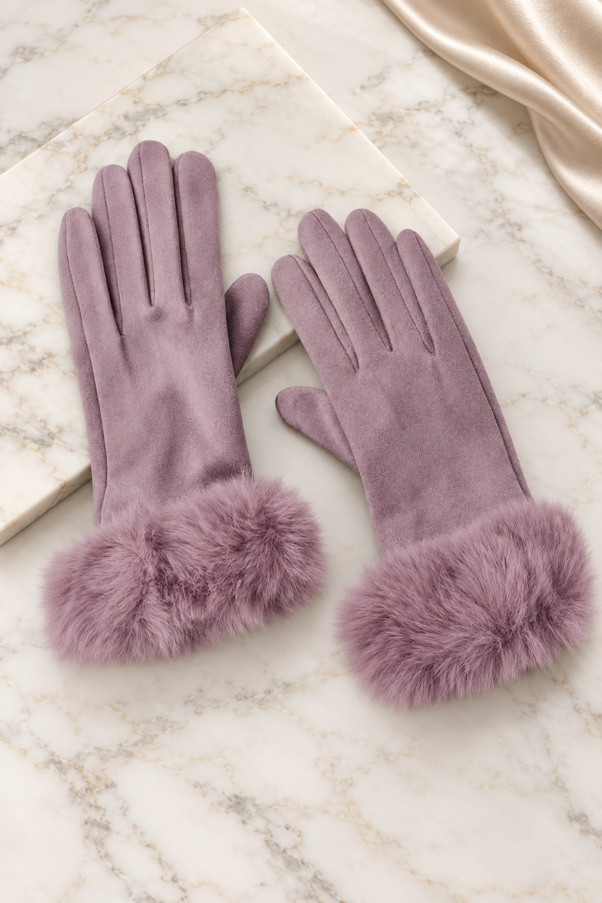 A pair of mauve purple faux-suede gloves with fluffy faux-fur cuffs, displayed on a white marble surface with a cream satin ribbon.