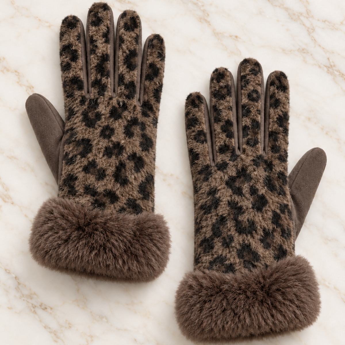 A pair of brown and black leopard-print knit gloves with solid brown suede-like fingertips and thick brown faux-fur cuffs, displayed on a light marble surface.