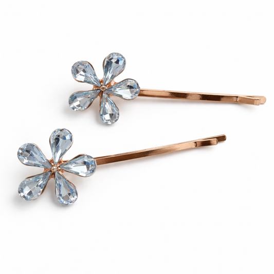 Two rose gold hair pins with flower-shaped blue gemstones on a white background