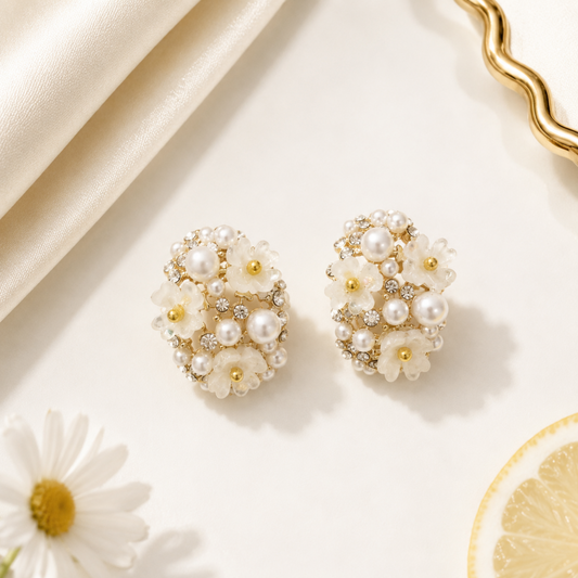 Pearl and gold earrings on a light background with flowers and fabric.