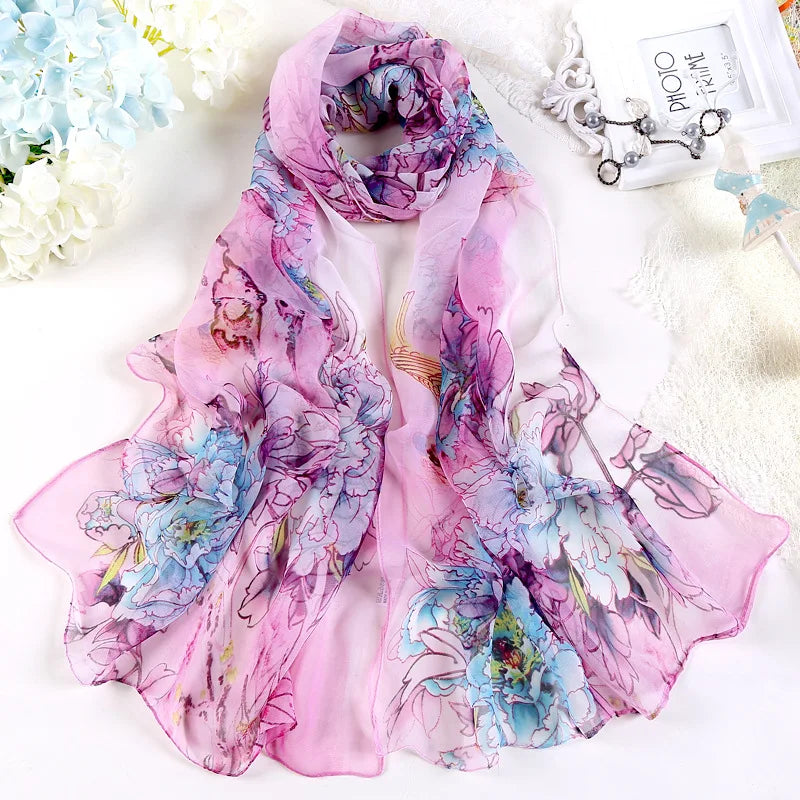 A lightweight pink scarf with a soft floral print laid out flat.