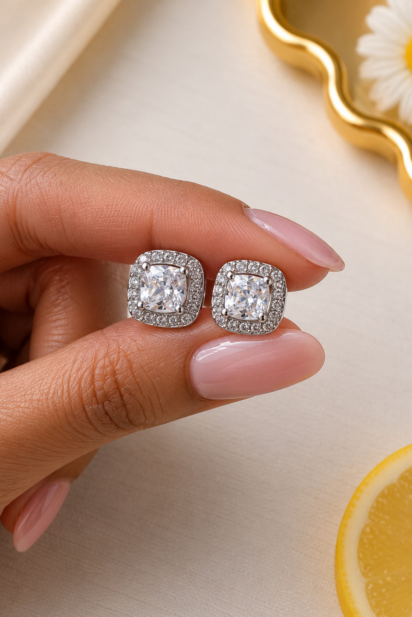 Silver earrings with clear stones held by a hand on a light background