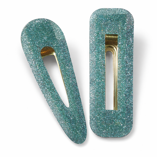 Two green glittery hair clips with gold hardware on a white background
