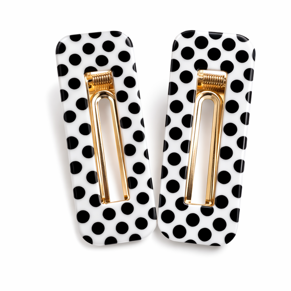 Pair of black and white polka dot hair clips with gold centers on a white background