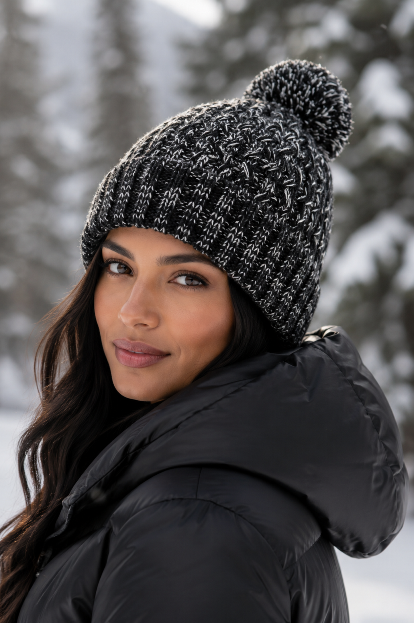 Woman wearing a black knit beanie with a pom-pom in a snowy forest setting