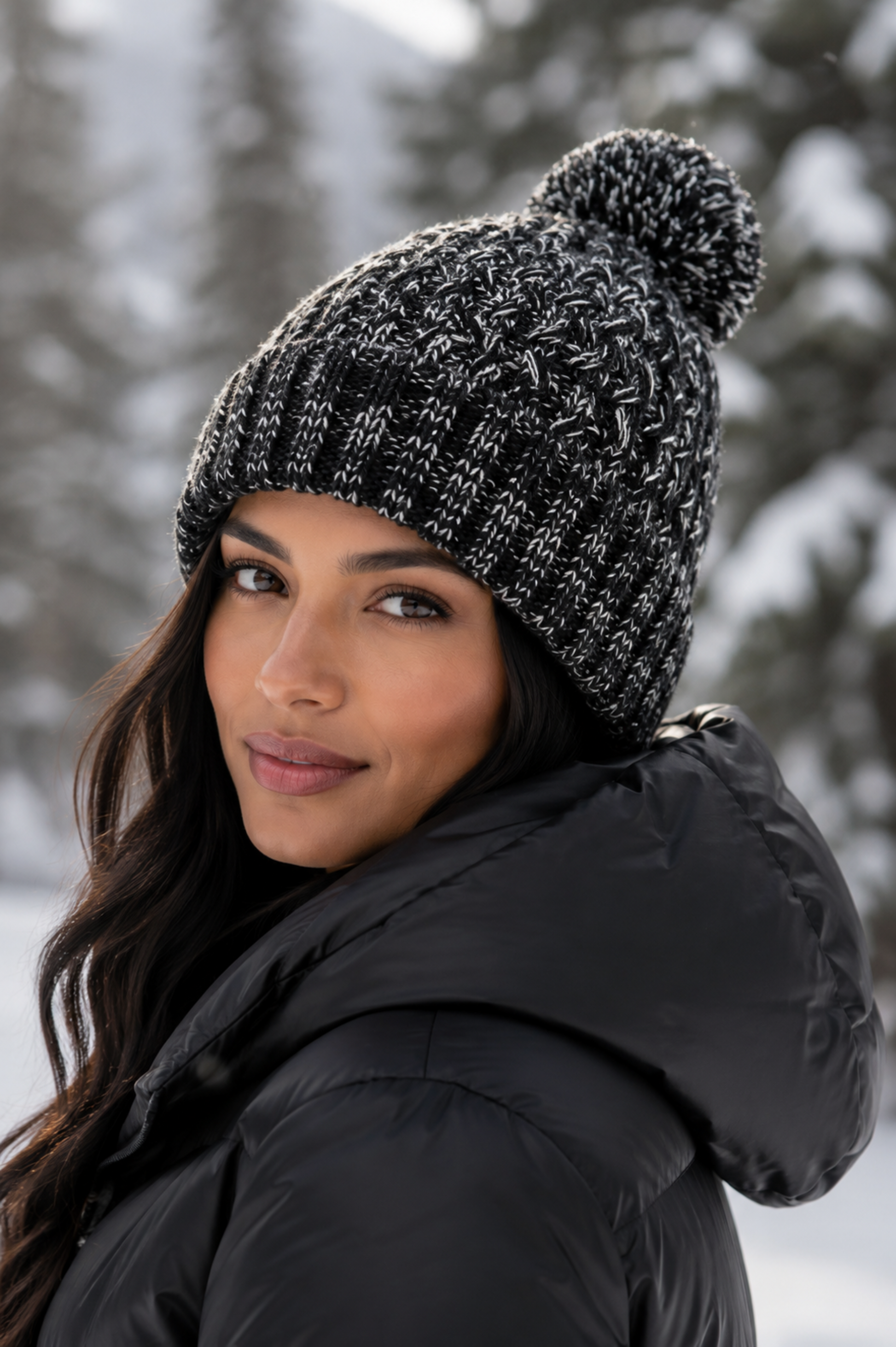 Woman wearing a black knit beanie with a pom-pom in a snowy forest setting