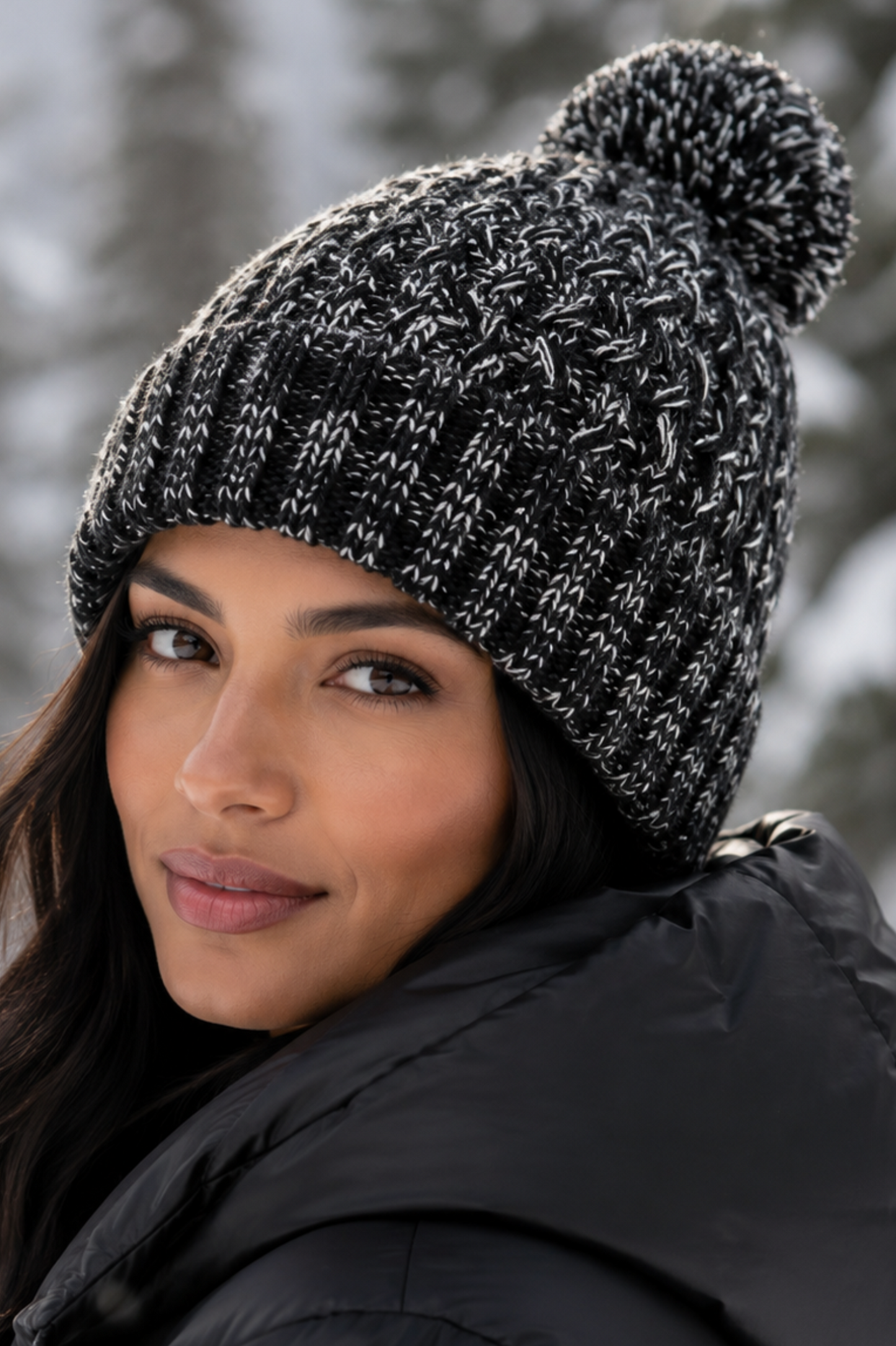 Woman wearing a black knit beanie with a pom-pom in a snowy forest setting