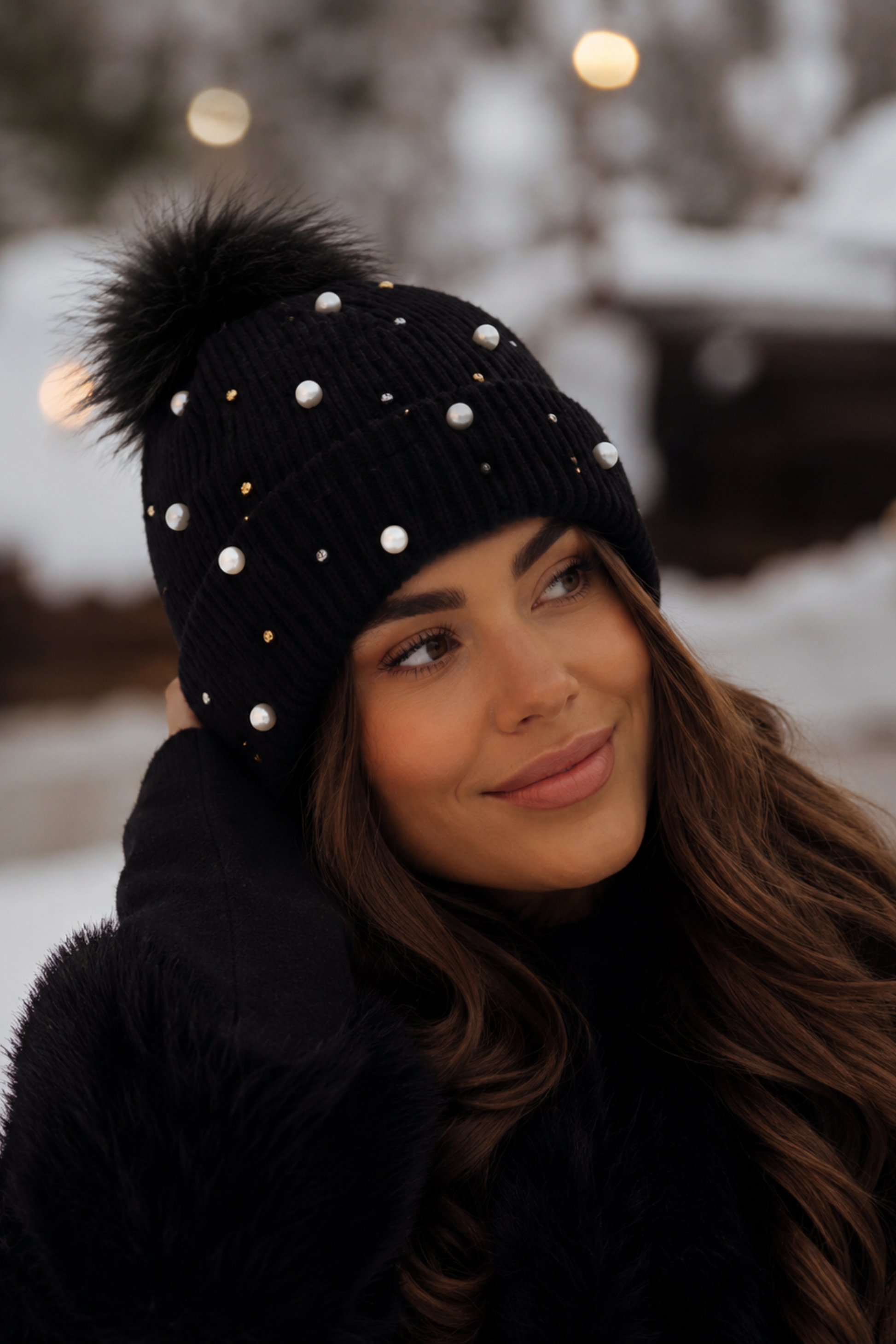 Woman wearing a black knit beanie with a pom-pom in a snowy outdoor setting