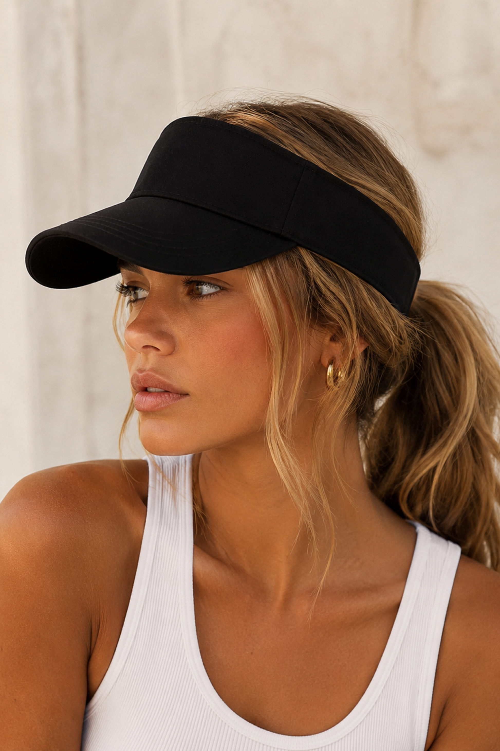 Woman wearing a black visor and white tank top against a neutral background