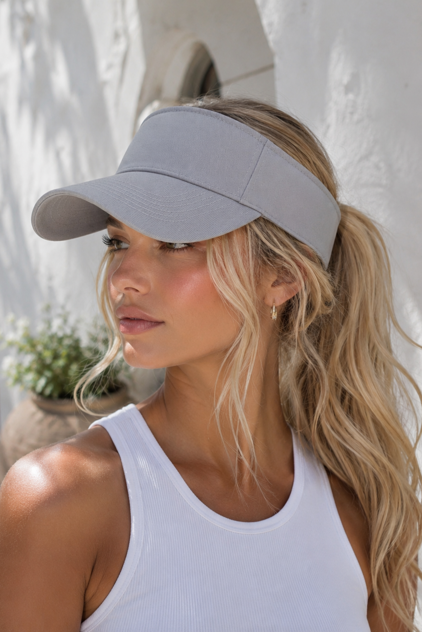 Woman wearing a gray visor outdoors with a white wall and plant in the background