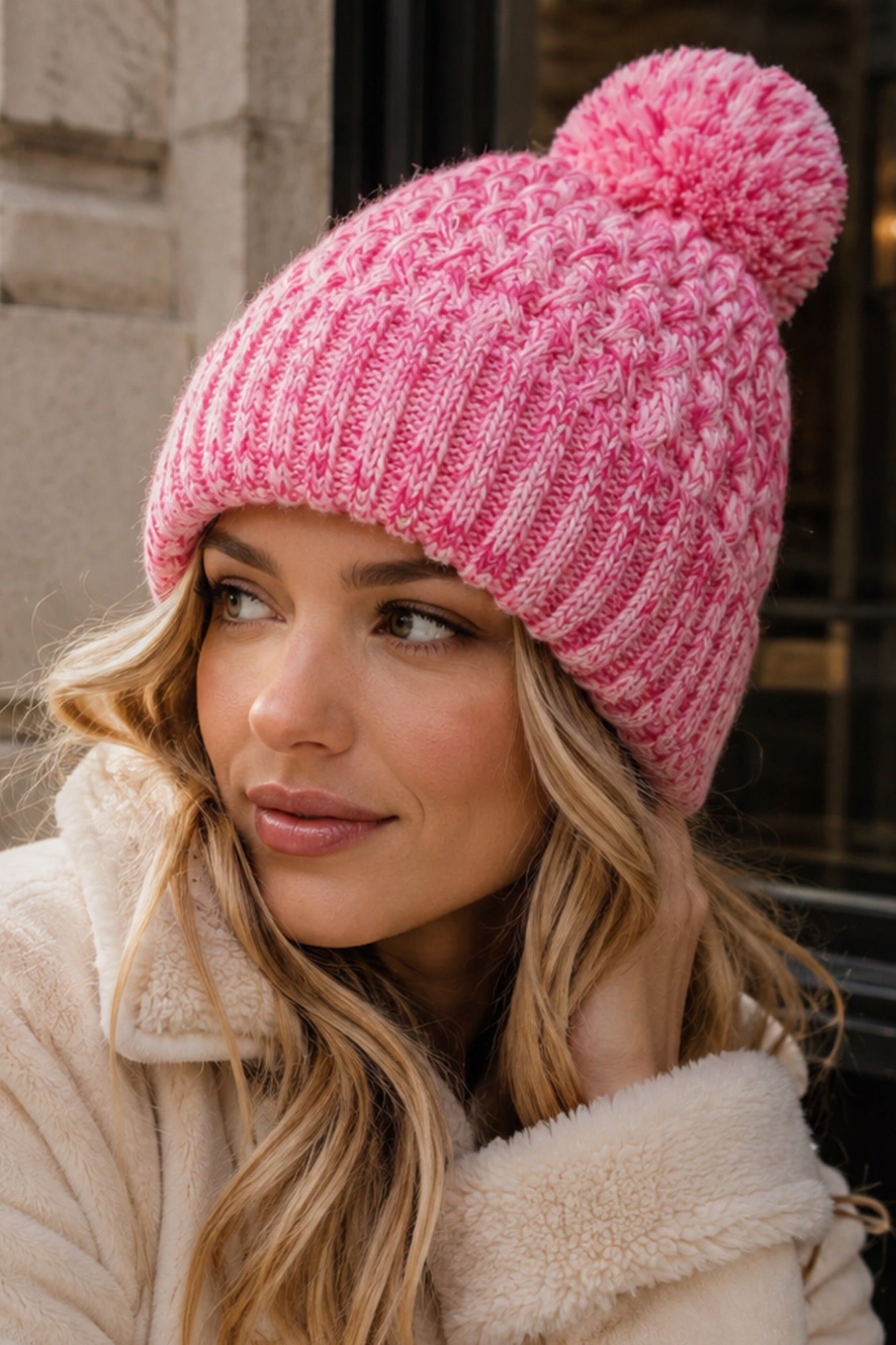 Woman wearing a pink knitted beanie and beige coat outdoors.