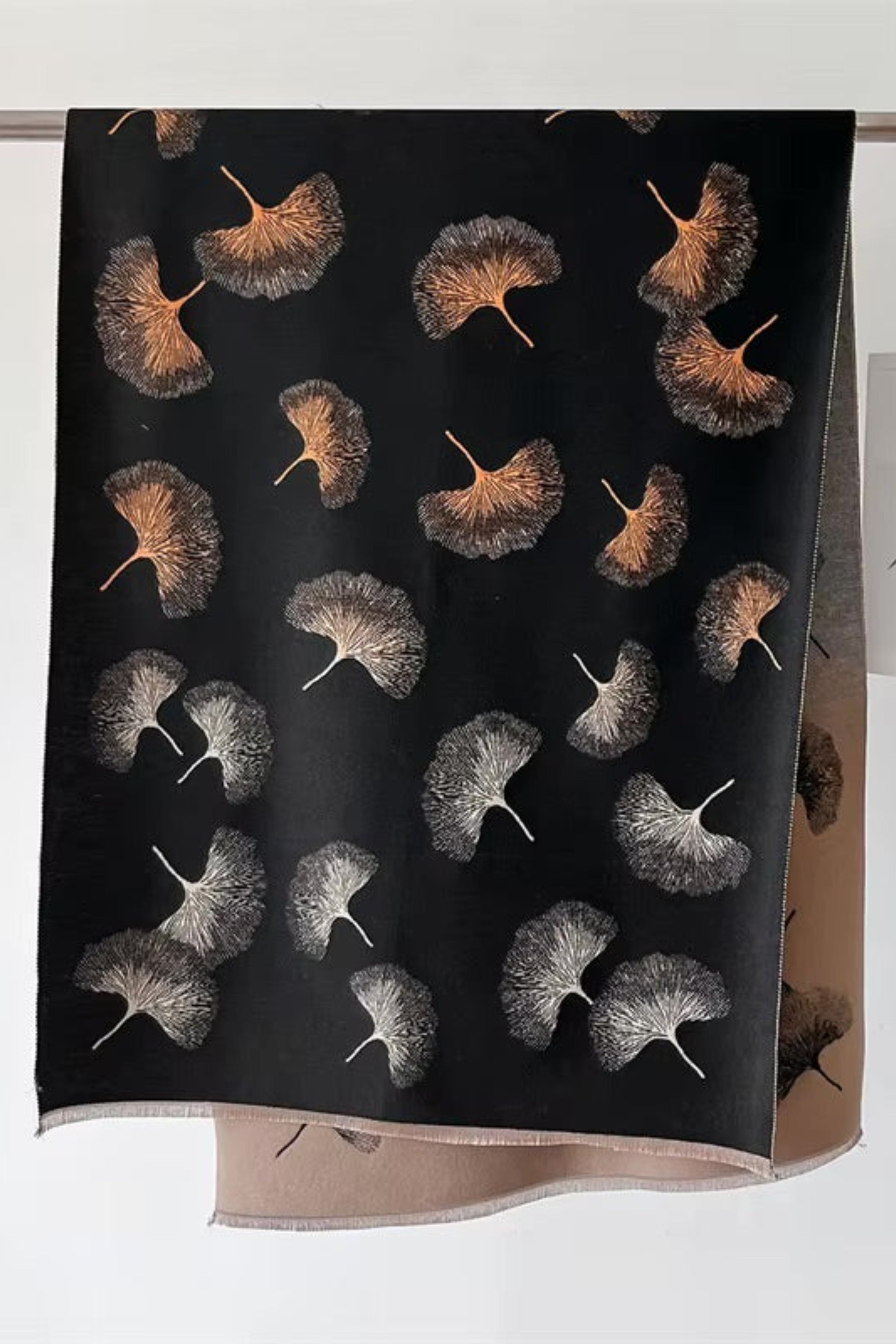 Black scarf with nature-themed pattern hanging on a rack